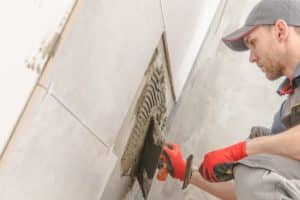 Tile installer carefully placing 12x12 ceramic tiles in a shower